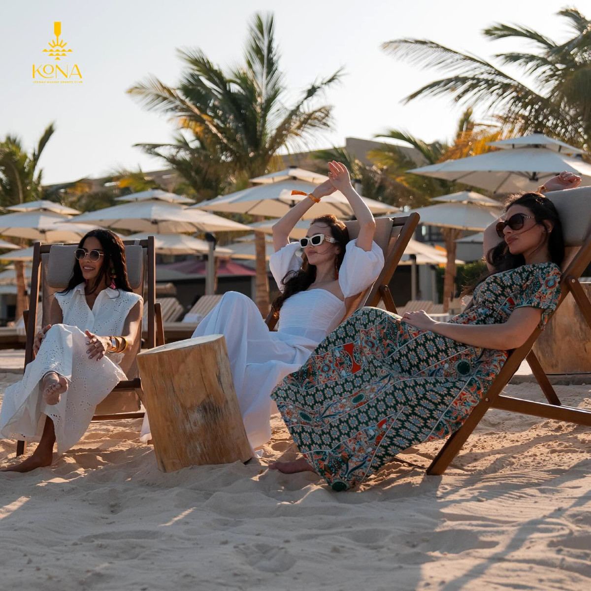 Three guests relaxing in deck chairs on the sand beneath parasols at Kona Marine Sport Club