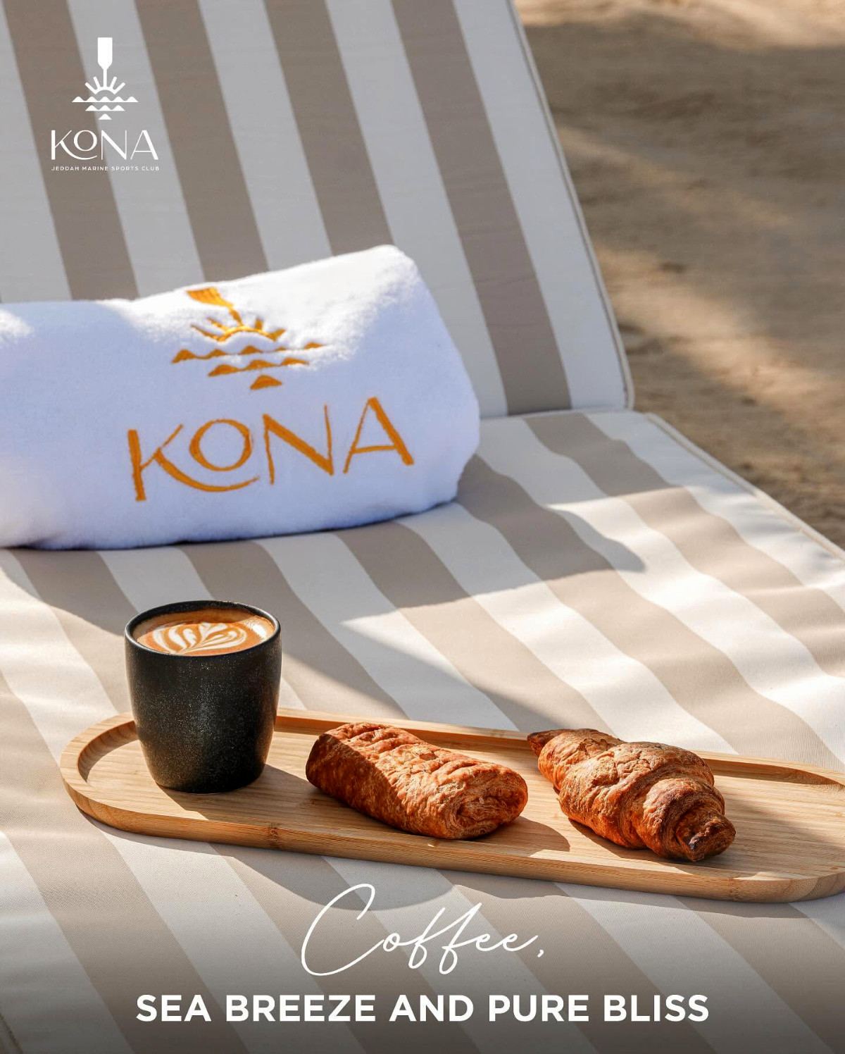 Latte and pastries by a Kona towel on a lounger, captioned “Coffee, sea breeze and pure bliss”