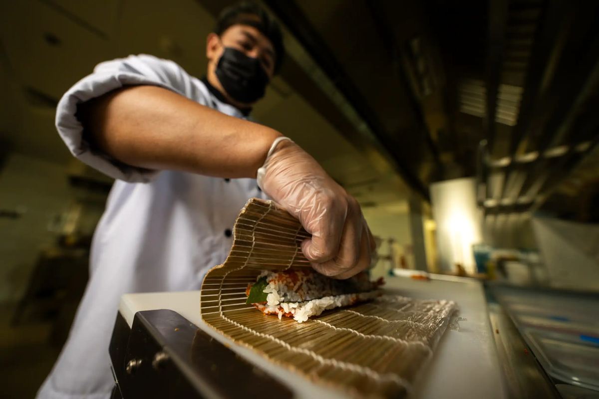 Chef rolling sushi with a bamboo mat in the kitchen at Kona Marine Sport Club