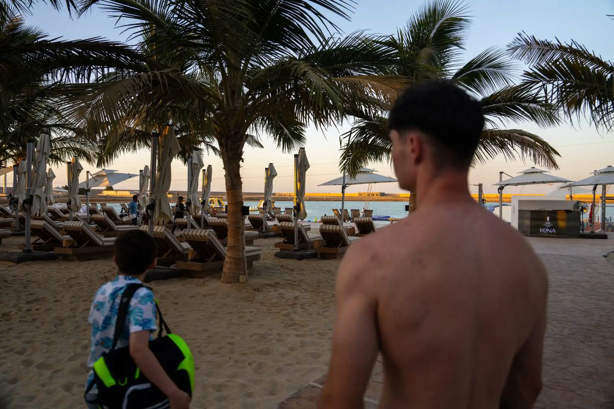 Guests heading toward palm-shaded loungers and parasols on the beach at Kona Marine Sport Club