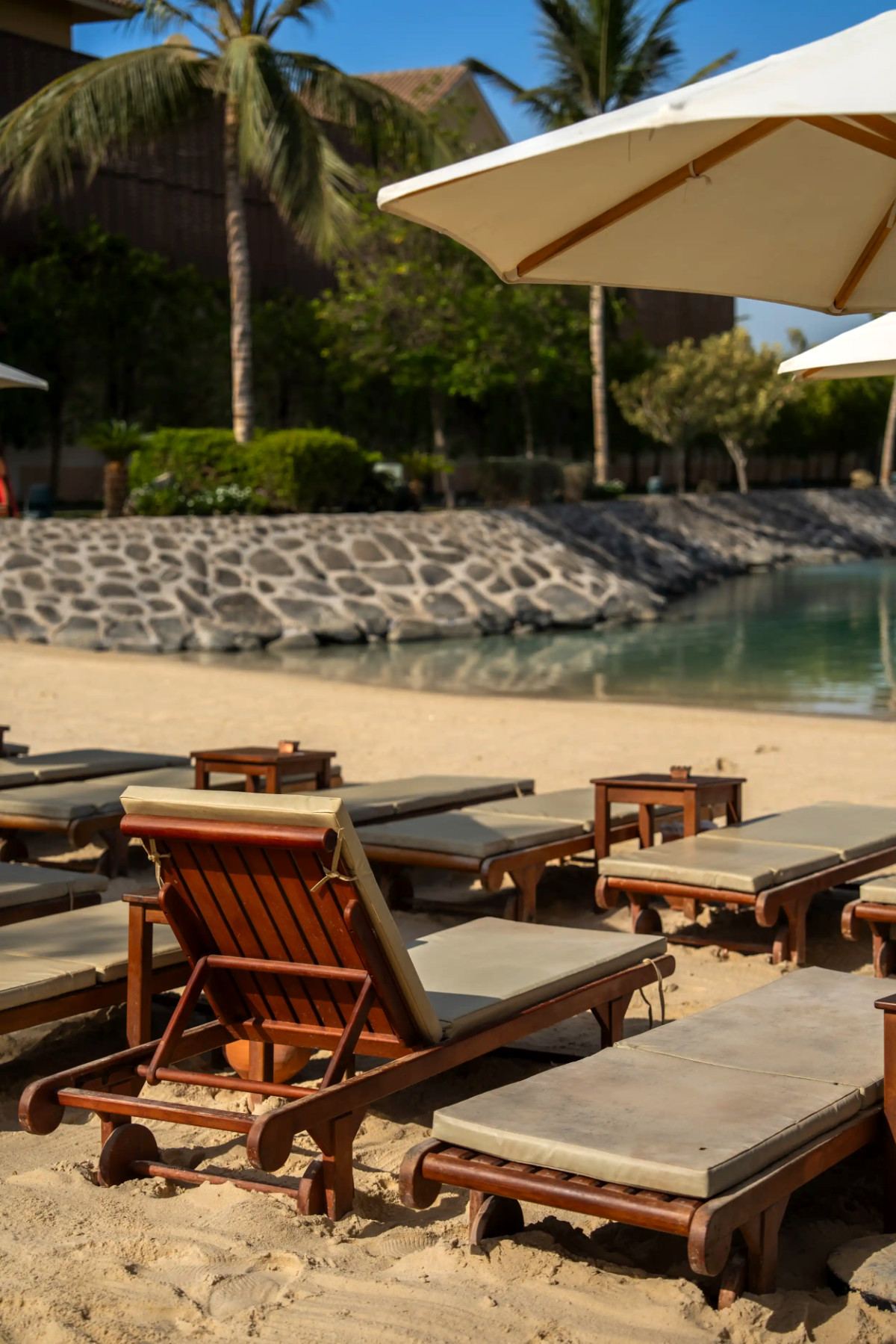 Close-up of cushioned wooden sun loungers on the sand by the lagoon at La Maison D’Obhur