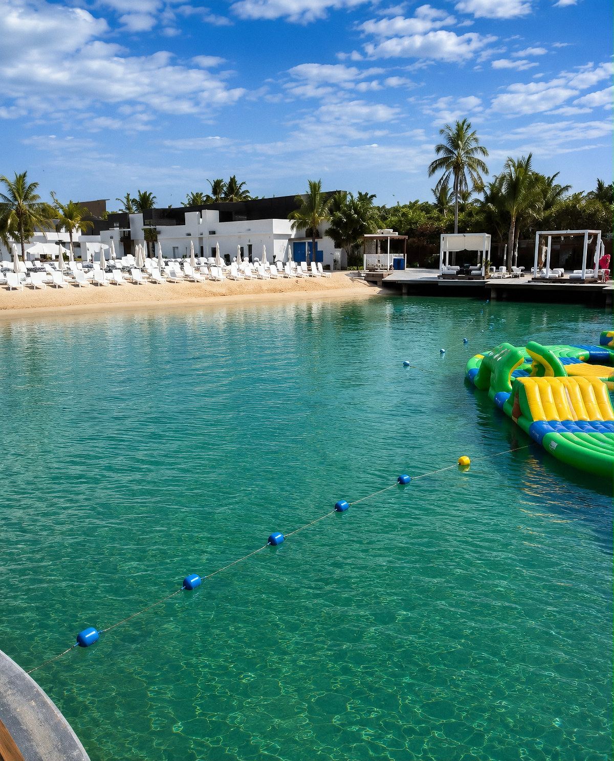 Turquoise lagoon with an inflatable water park, sunbeds and cabanas at Mangrove Beach Resort