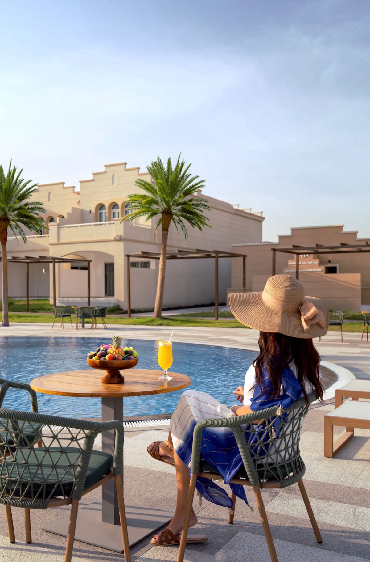 Guest in a sun hat relaxing poolside with fresh fruit and juice at Rixos Obhur Jeddah