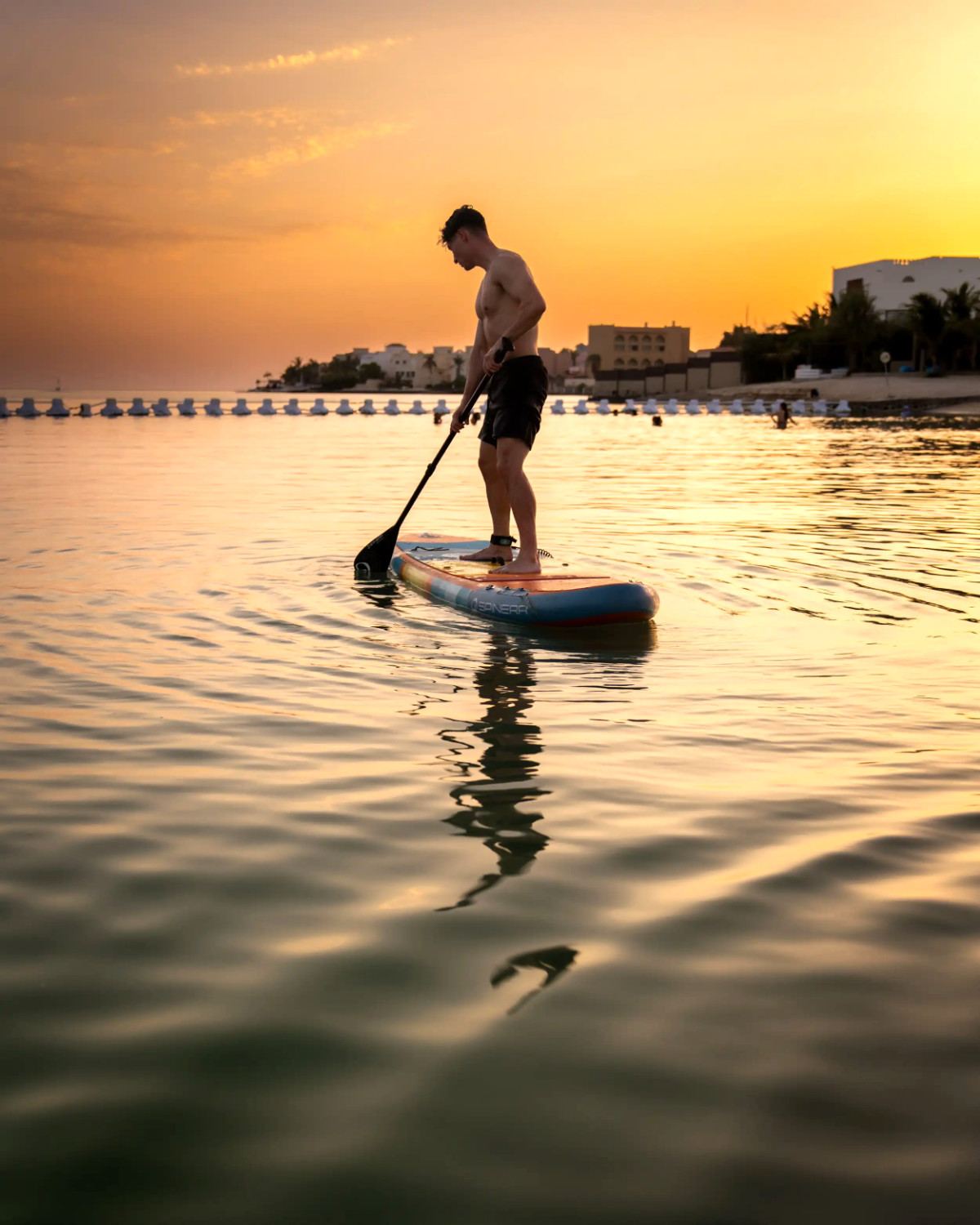 A paddle boarder standing on calm, glassy water as the sun sets