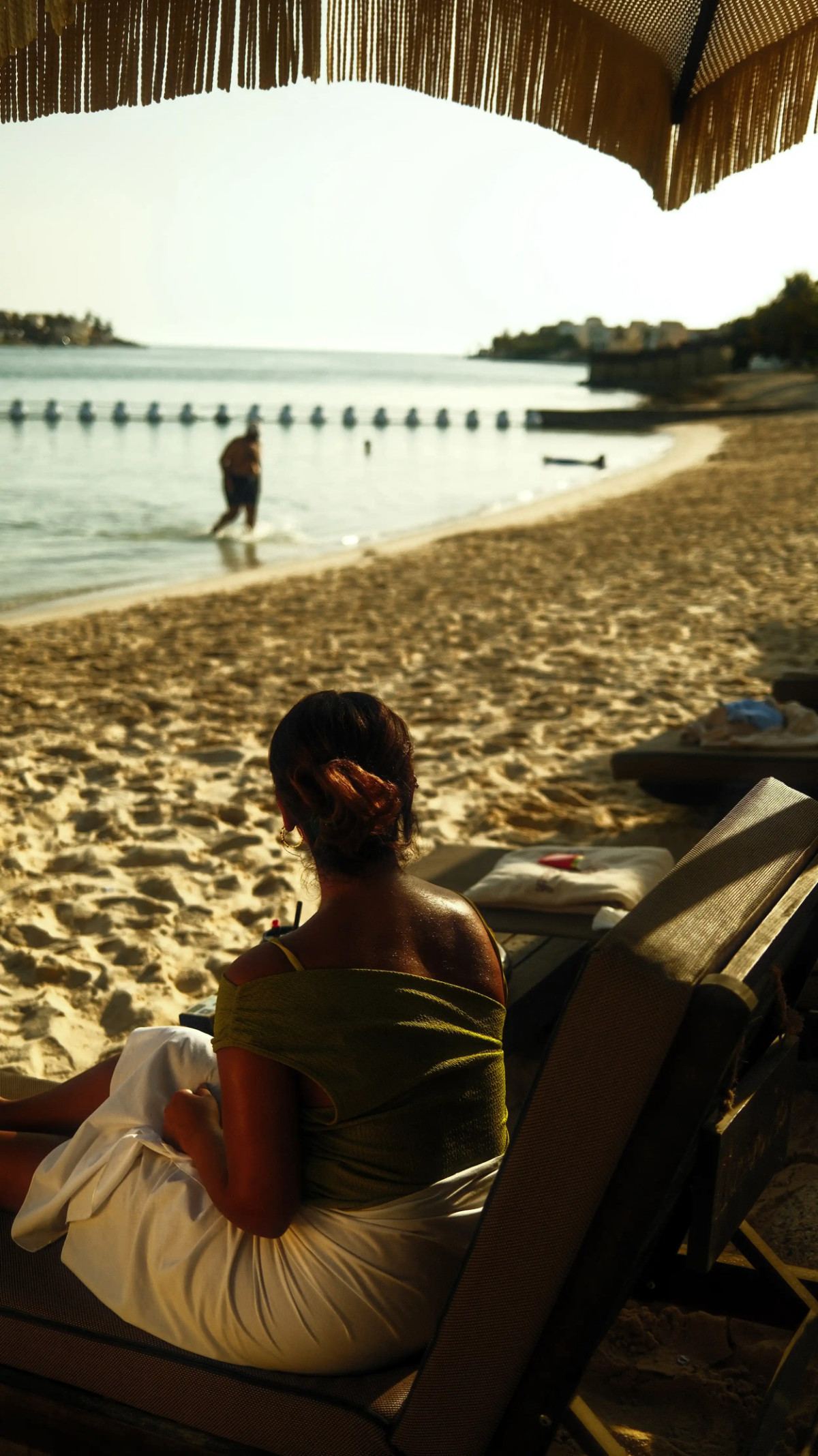 Guest relaxing under a fringed parasol overlooking the sandy shore at Shades Beach Club