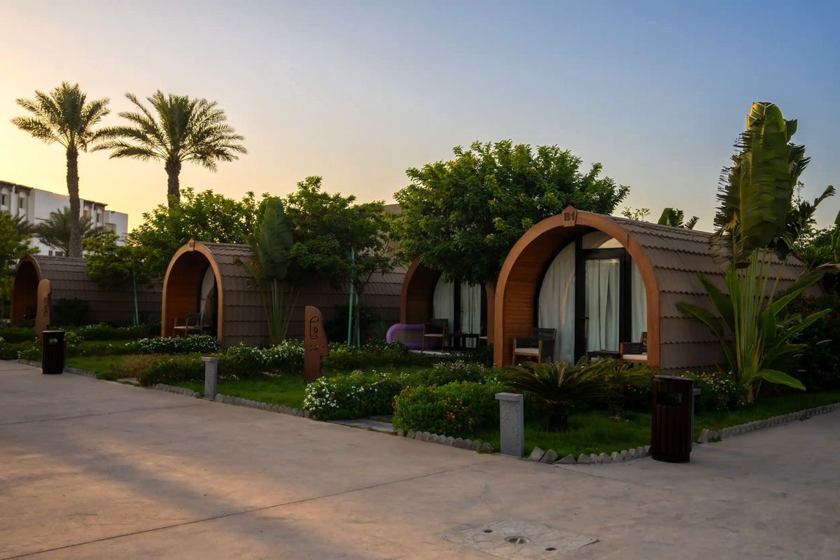 Arched wooden pod chalets set in landscaped gardens at sunset at Shades Beach Club