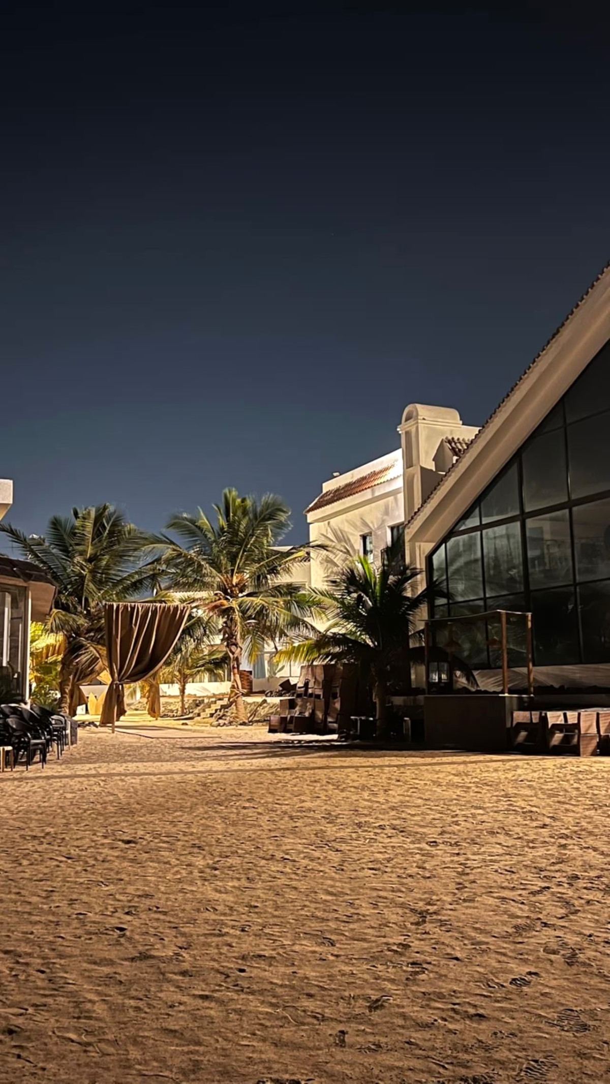 Siyal Resort’s sandy beachfront at night with palms, a draped cabana and a glass-fronted lounge