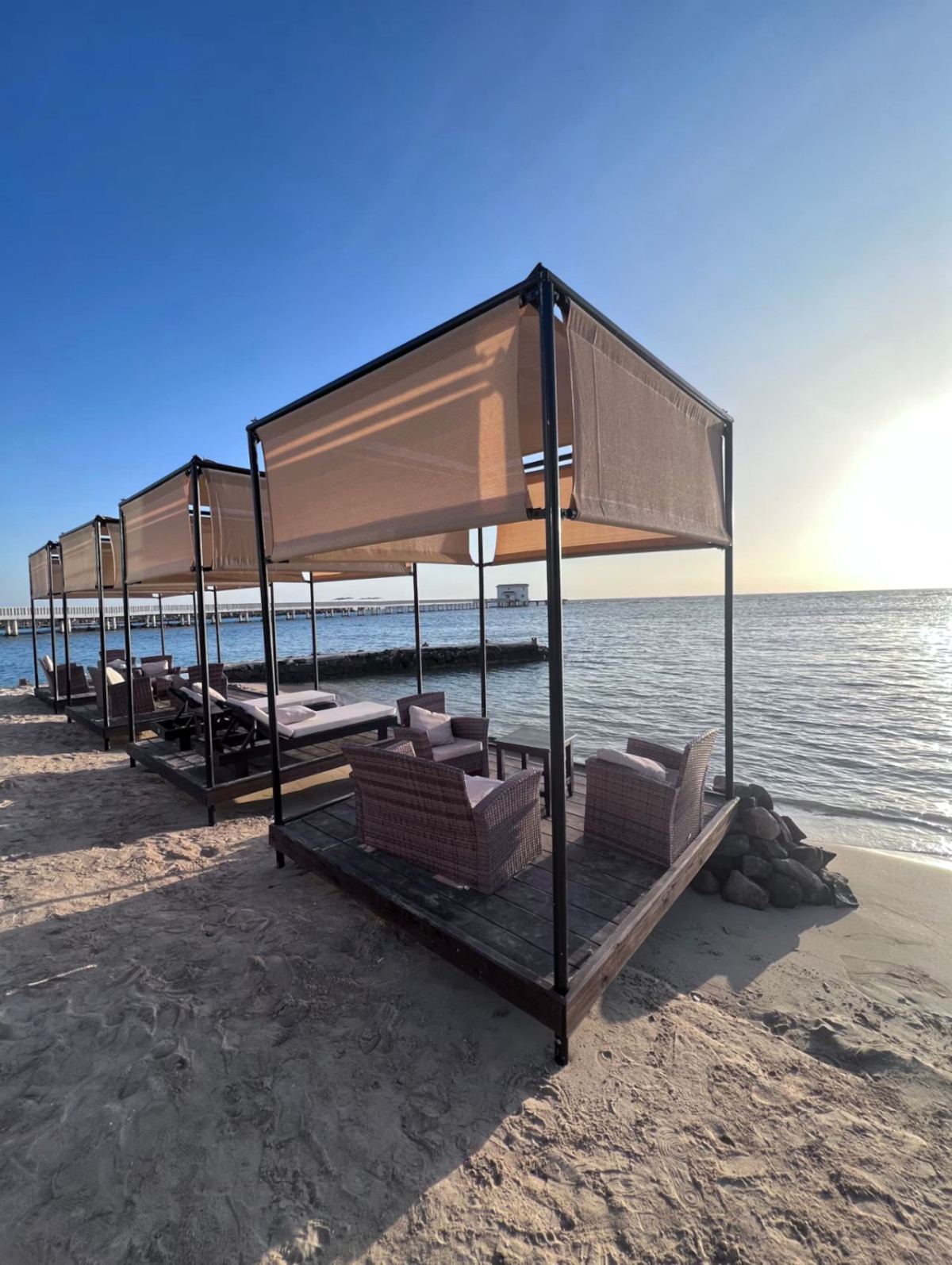 Shaded beach cabanas with wicker seating at the water’s edge at Siyal Resort