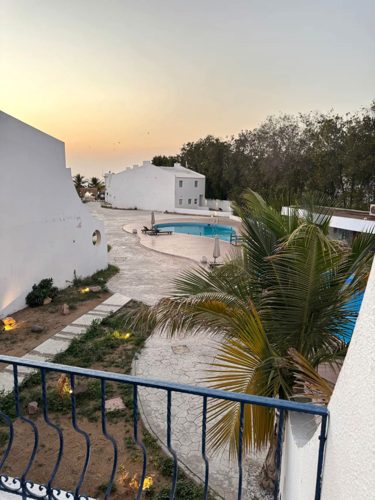 Dusk view from a balcony over Siyal Resort’s pool, palms and white villas